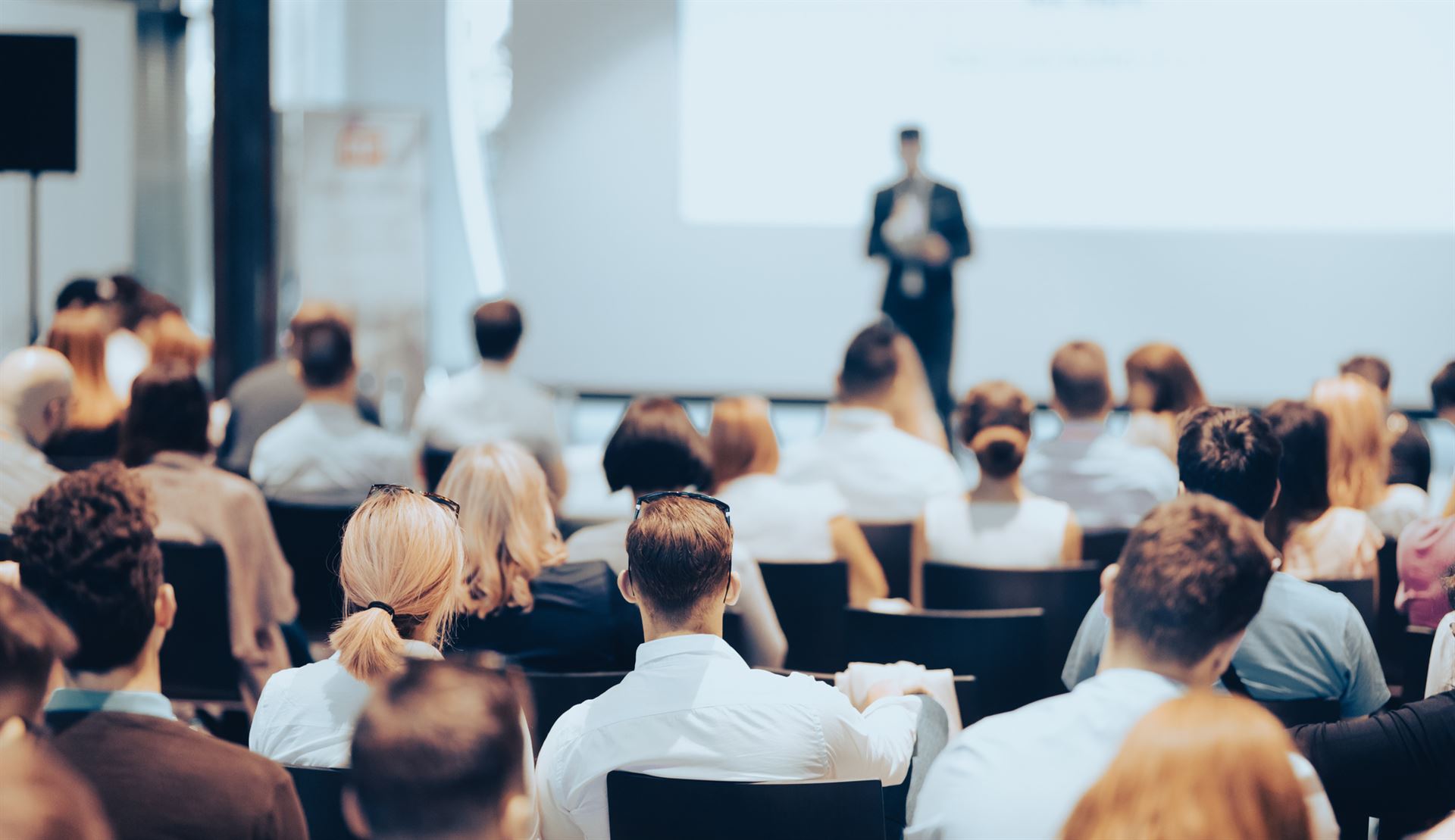 Mówca wygłaszający przemówienie w sali konferencyjnej na imprezie biznesowej. Widok z tyłu osób na widowni